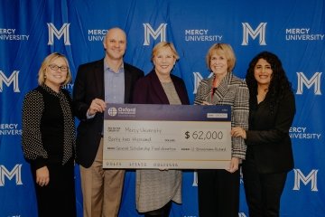 Oxford International Education Group and Mercy University officials pose in front of large cardboard check symbolic of the $62, 000 donation they made to the university