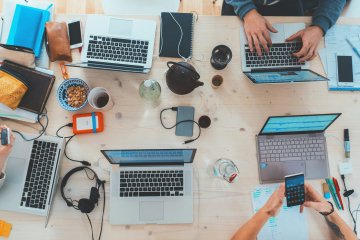 People sitting around a table with various laptops and devices being used.