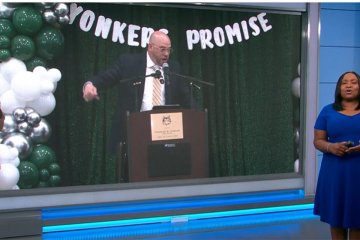 News 12 anchor with Yonkers Promise announcement in the background