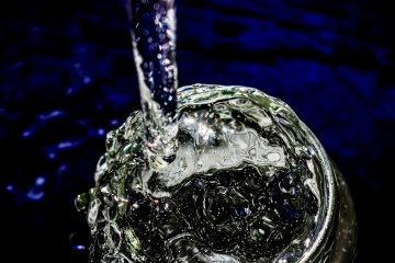 Photo of water pouring into a clear glass with a dark blue background