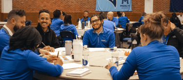 Teams of counselors in blue shirts at tables