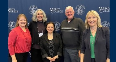 Faculty pose in front of Mercy College sign  